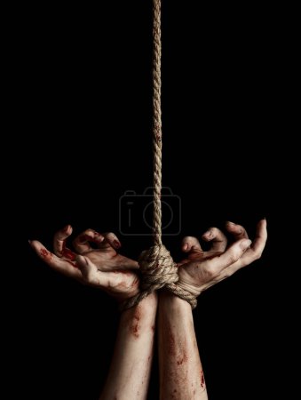 Téléchargez les photos : Les mains de la femme avec des taches sanglantes attachées avec une corde sur fond noir - en image libre de droit