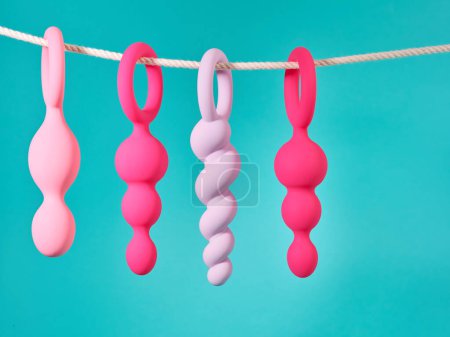 Foto de Conjunto de juguetes sexuales de color rosa colgando de una cuerda sobre fondo azul turquesa - Imagen libre de derechos