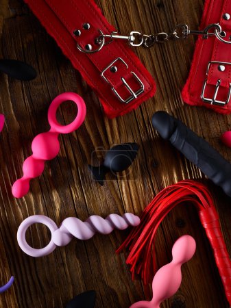 Foto de Sex toys including cuffs, whip, anal plugs, dildo over aged wooden background - Imagen libre de derechos
