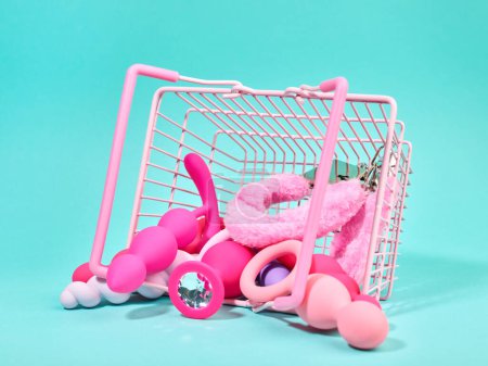 Téléchargez les photos : Femme rose jouets sexuels dans le chariot d'achat sur fond turquoise - en image libre de droit