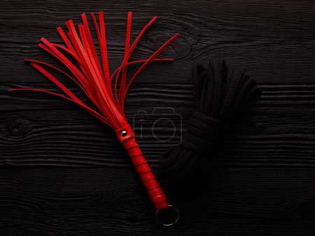Téléchargez les photos : Fouet rouge et corde noire pour un jeu de rôle BDSM sur fond en bois noir - en image libre de droit
