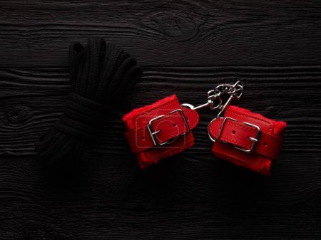 Foto de Fondo BDSM con esposas esponjosas de color rojo brillante y cuerda para atar - Imagen libre de derechos