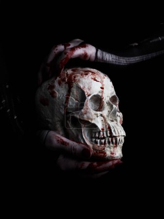 Foto de Manos ensangrentadas de una bruja sosteniendo cráneo humano sobre fondo negro - Imagen libre de derechos