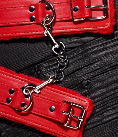 Photo for Red handcuffs over black wooden backdrop. bdsm background - Royalty Free Image