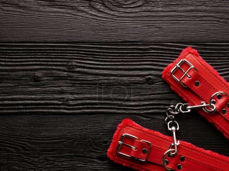 Photo for Red handcuffs over black wooden backdrop. bdsm background - Royalty Free Image