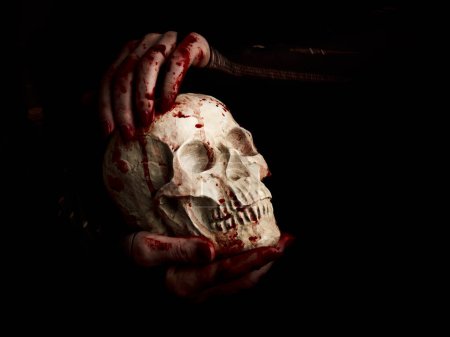 Téléchargez les photos : Mains sanglantes d'une sorcière tenant un crâne humain sur fond noir - en image libre de droit