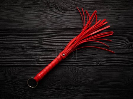 Bright red handcuffs and red whip over black wooden background magic mug #710526456