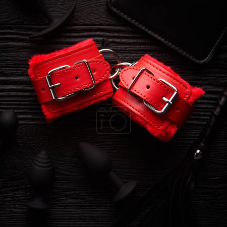 Foto de Esposas rojas brillantes y látigo rojo sobre fondo de madera negro - Imagen libre de derechos