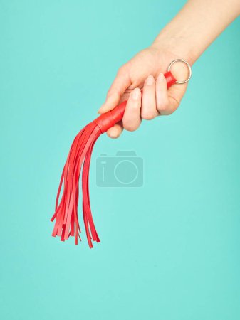 Foto de Látigo rojo para juegos de rol para adultos en la mano de la mujer sobre fondo azul turquesa - Imagen libre de derechos