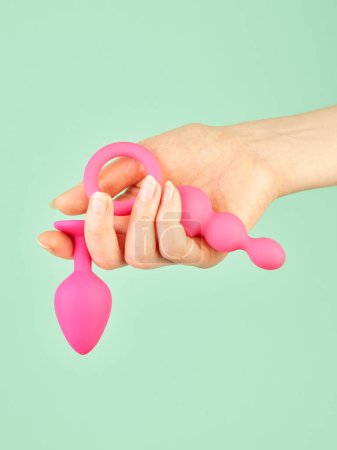 Foto de La mano de la mujer sosteniendo juguetes sexuales para adultos sobre fondo de menta - Imagen libre de derechos