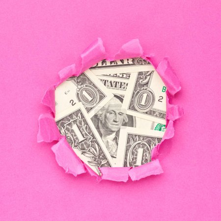 Téléchargez les photos : Des billets en dollars dans le trou de papier rose déchiré. Concept d'entreprise féminine - en image libre de droit