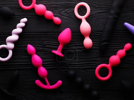 Téléchargez les photos : Anal plugs and dildo in different shades of pink over black wooden background - en image libre de droit