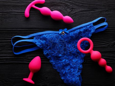 Téléchargez les photos : Culotte bleue lumineuse et différents jouets sexuels sur fond en bois noir - en image libre de droit