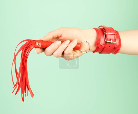 Photo for Woman's hand holding red whip for adult role play games over mint background - Royalty Free Image
