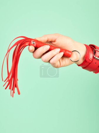 Foto de La mano de la mujer sosteniendo látigo rojo para juegos de rol para adultos sobre fondo de menta - Imagen libre de derechos