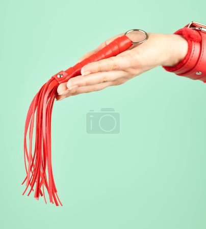 Foto de Woman's hand holding red whip for adult role play games over mint background - Imagen libre de derechos