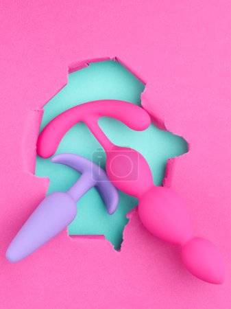 Photo for Anal plug and dildo sex toys over hole in pink paper background - Royalty Free Image