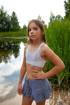 Photo for Athletic teenage girl walks near the lake in nature, summer season, cloudy sky - Royalty Free Image