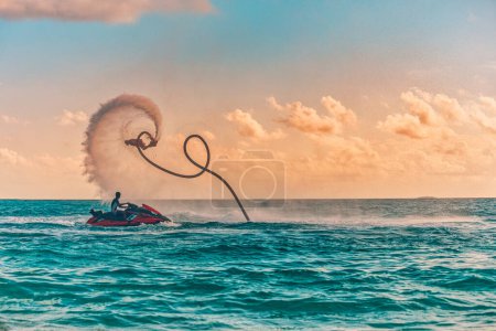 Photo for Silhouette of a fly board rider at sea. Professional rider do tricks in the blue lagoon. Tropical watersport equipment. Sunset sea view, summer outdoor sport, recreational activity, amazing splash - Royalty Free Image