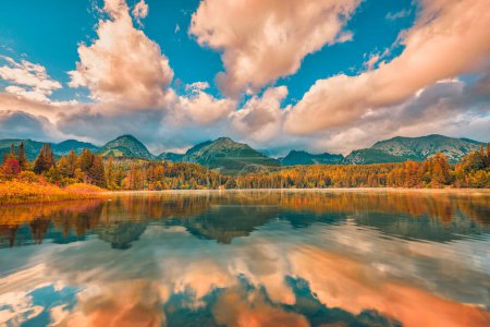 Foto de Hermoso paisaje otoñal. Fondo de viaje idílico, concepto de belleza en la naturaleza. Montañas Tatra árboles de bosque amarillo anaranjado, vista al lago puesta de sol. Increíbles nubes de cielo y caída de agua reflejo panorama - Imagen libre de derechos