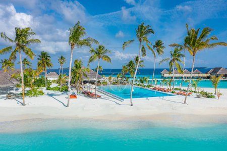 Photo for Beachside tourism landscape. Luxurious beach resort poolside, swimming pool and beach chairs or loungers, umbrellas with tropical palm trees and blue sky. Summer travel and vacation background concept - Royalty Free Image