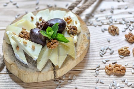 Photo for Different types of cheeses on a wooden plank with plums and a mint leaves on a table - Royalty Free Image