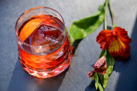 Téléchargez les photos : Cocktail alcoolisé rouge dans un beau verre sur fond sombre avec des fleurs - en image libre de droit
