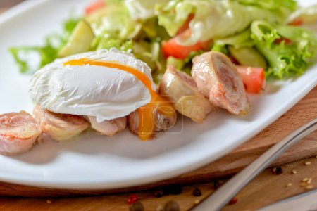 Téléchargez les photos : Gros poulet avec une salade fraîche sous un œuf poché dans une assiette ronde blanche sur une table dans un restaurant - en image libre de droit