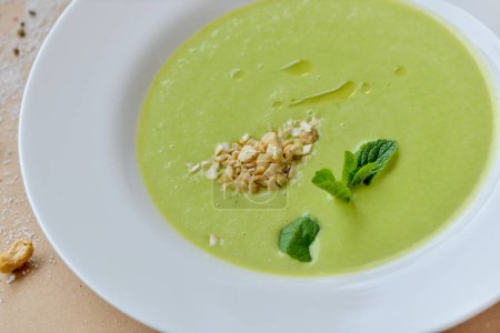 Téléchargez les photos : Soupe crème verte dans une assiette blanche décorée de feuilles de menthe - en image libre de droit