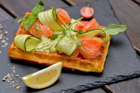 Téléchargez les photos : Gaufre de petit déjeuner avec saumon et concombre sur une ardoise noire sur la table - en image libre de droit