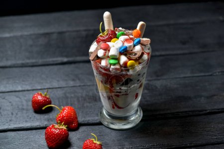 Foto de Postre de leche en un vaso con fresas de chocolate y dulces sobre un fondo negro - Imagen libre de derechos