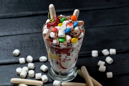 Téléchargez les photos : Dessert au lait dans un verre avec des fraises au chocolat et des bonbons sur fond noir - en image libre de droit