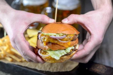 Téléchargez les photos : Mains avec grand hamburger avec falafel sur une planche avec frites - en image libre de droit