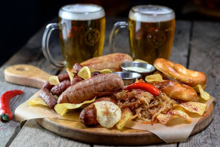 Foto de Tazas de cerveza con pretzels, bratwurst, chucrut y pimientos en la mesa de madera - Imagen libre de derechos