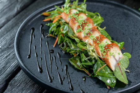 Téléchargez les photos : Savoureux poisson grillé et salade sur assiette noire - en image libre de droit