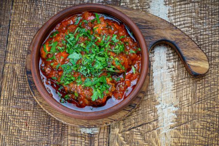 Téléchargez les photos : Plat de viande géorgien en sauce tomate dans une poêle en argile sur la table - en image libre de droit
