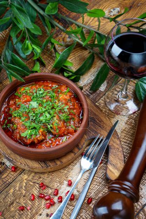 Téléchargez les photos : Plat de viande géorgien en sauce tomate dans une poêle en argile sur la table avec du vin - en image libre de droit