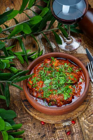 Téléchargez les photos : Plat de viande géorgien en sauce tomate dans une poêle en argile sur la table avec du vin - en image libre de droit