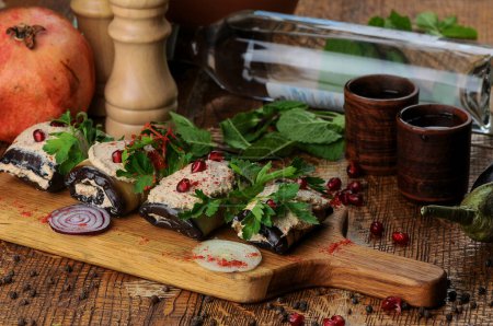 Photo for Georgian appetizer of eggplant in rolls with filling sprinkled with pomegranate seeds on the table with chacha and plant - Royalty Free Image