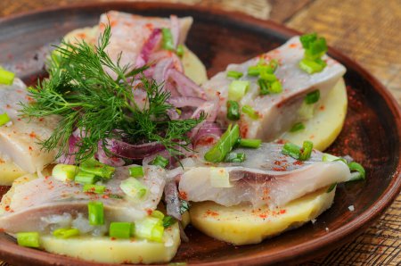Foto de El filete del arenque a las patatas con la cebolla y la verdura en el plato de barro - Imagen libre de derechos