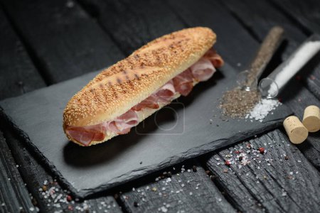 Téléchargez les photos : Sandwich aux saucisses et épices sur une planche à découper. sur fond noir - en image libre de droit