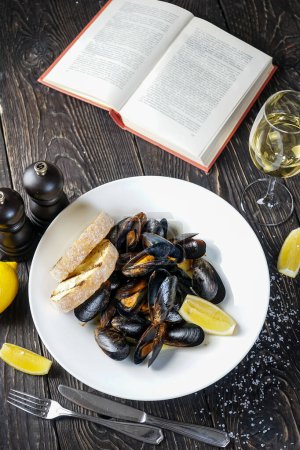 Photo for Boiled mussels in a plate with lemon and bruschetta with book - Royalty Free Image