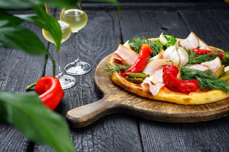 Photo for Pizza with ham, pickled cucumbers, garlic , red peppers and cheese on a wooden table. - Royalty Free Image