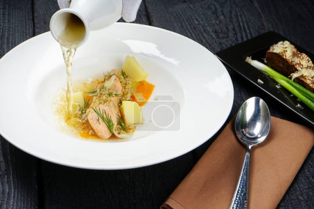 Téléchargez les photos : Main avec soupe de saumon aux légumes dans une assiette blanche et pain - en image libre de droit