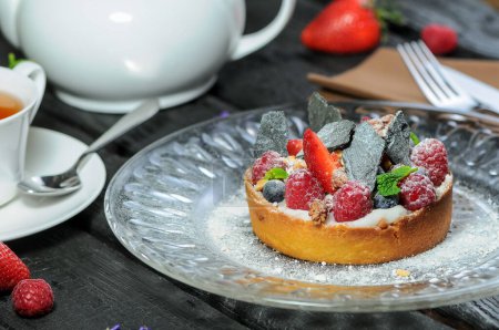 Foto de Tarta tarta con bayas, frutas y té en el fondo, de cerca - Imagen libre de derechos
