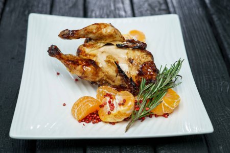 Photo for Roasted chicken  with spices and tangerine on a black plate. - Royalty Free Image