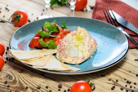 Téléchargez les photos : Houmous aux tomates et pain pita sur une assiette bleue sur un fond en bois - en image libre de droit