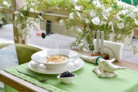 Foto de Avena con arándanos y frutos secos en un plato blanco en la terraza con flores - Imagen libre de derechos