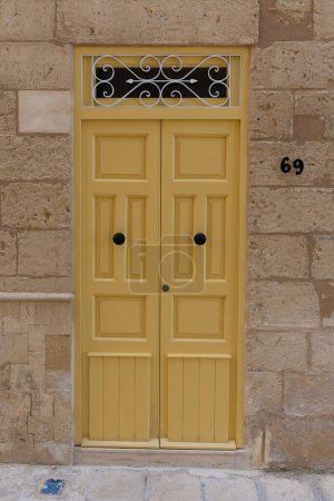 Foto de Yellow door and number 69 on an exterior brick wall. The building is somewhere in Malta. - Imagen libre de derechos