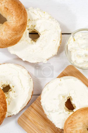 Photo for Bagel sandwich with fresh cream cheese for breakfast from above on a wooden board portrait format - Royalty Free Image